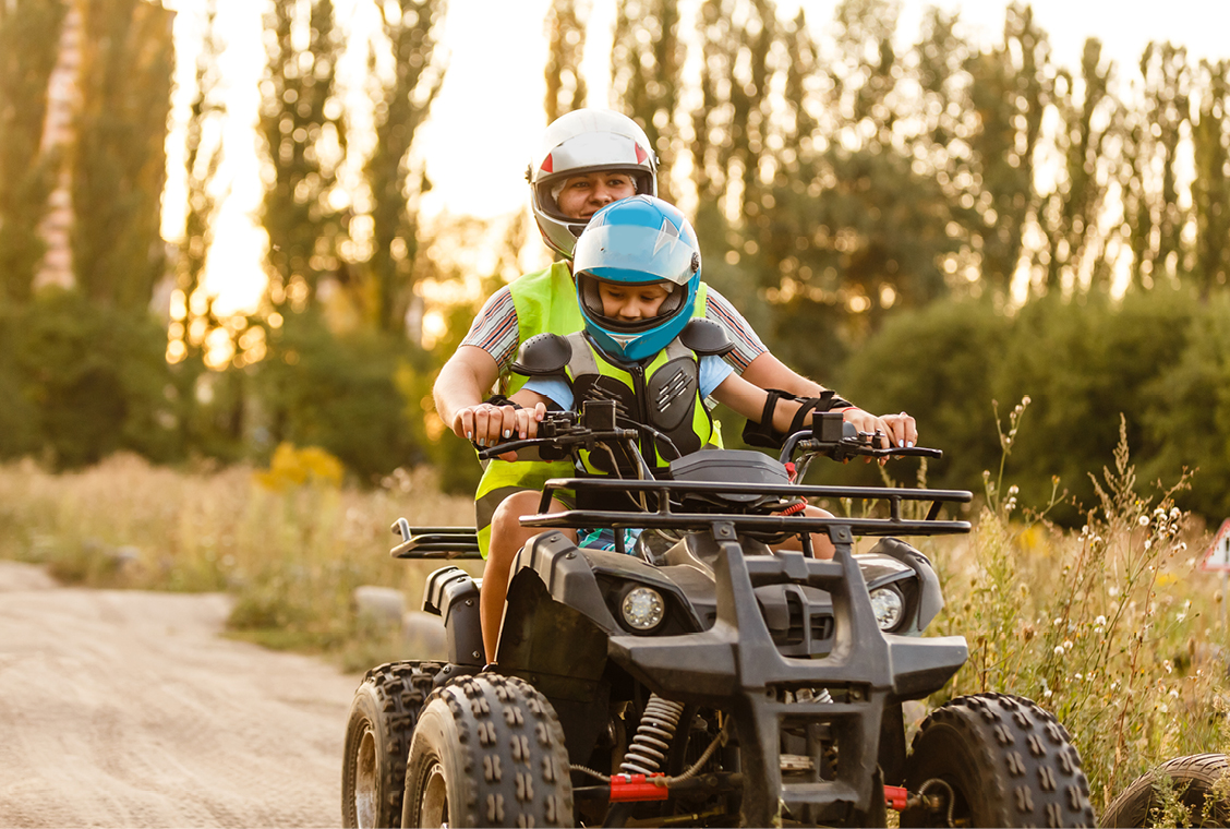 Father and son ride quad down dirt path outside.