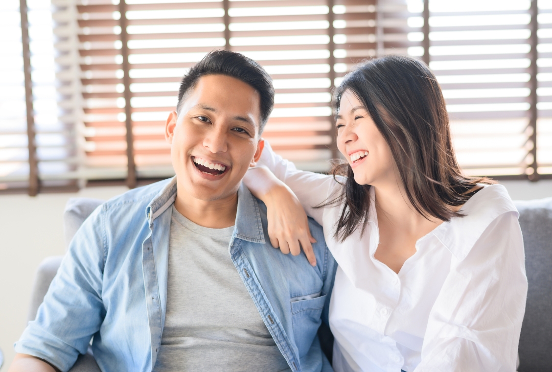 Couple sitting on couch in house smiling and laughing with each other